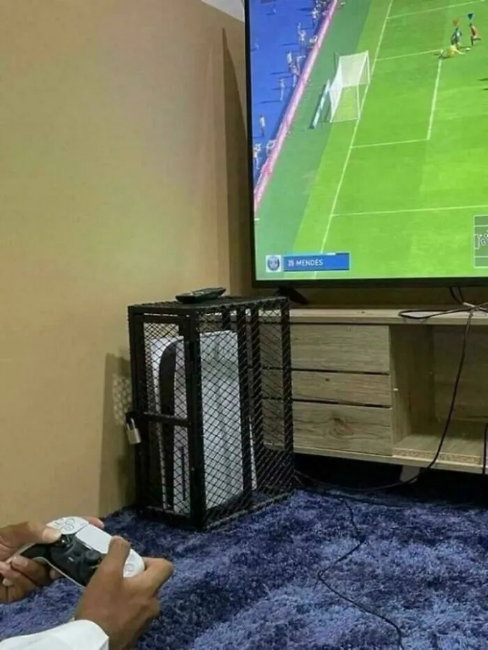 An unhinged image of a PS5 console locked in a cage, next to a TV showing a soccer game.