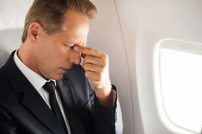 Frustrated man rubbing his temples, suffering from a plane seatmate from hell