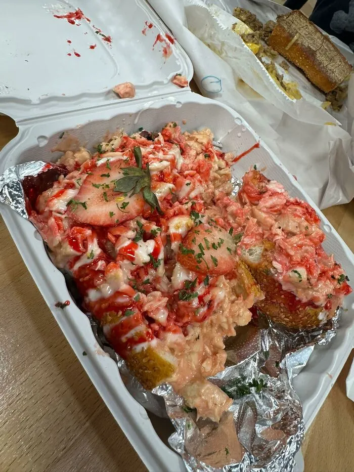 A chaotic strawberry lobster roll in a takeout box, illustrating unusual food combinations.