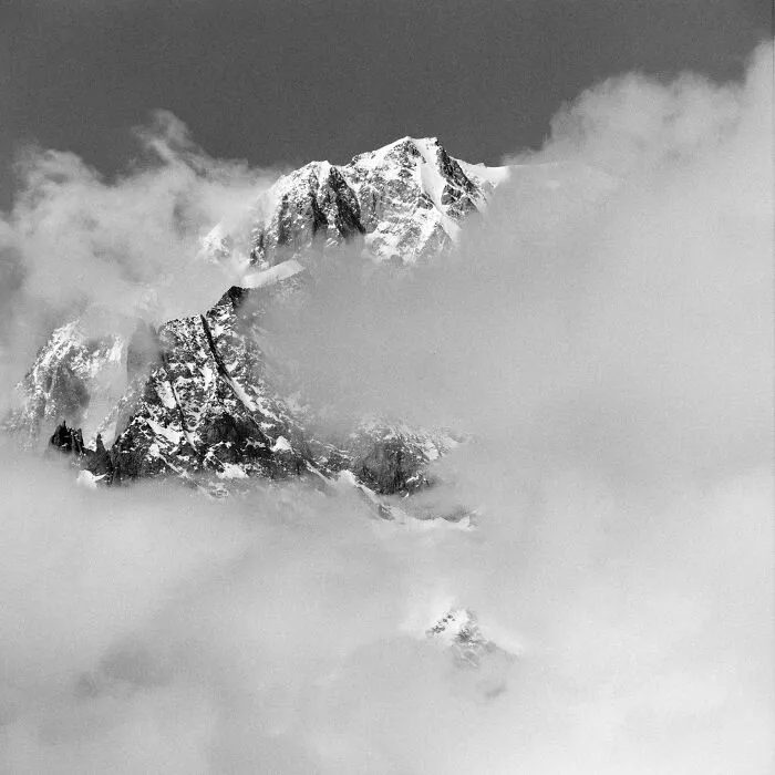 Black and white analog film photo of snow-covered mountain peak partly obscured by clouds