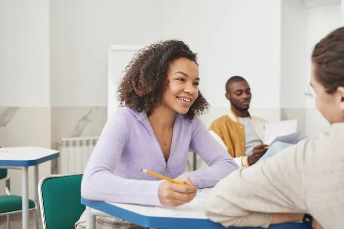 A smiling female student talking with classmates as teachers share stories