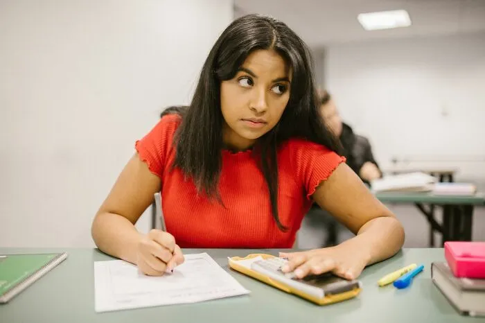 A student looking thoughtful in class while writing on a test paper, depicting moments of common sense