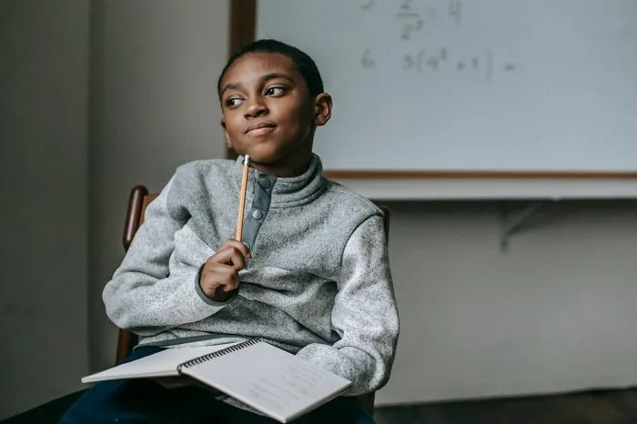 Pensive young boy holds a pencil in a classroom, representing teachers recall of student behavior