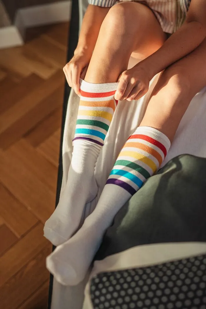 A person pulling up rainbow-striped socks, symbolizing a quirky student lacking common sense in class