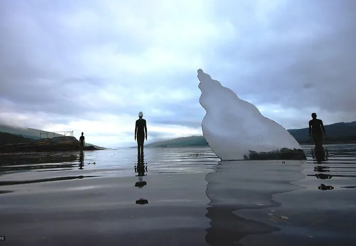 Series of reflective sculptures standing in shallow water under cloudy sky