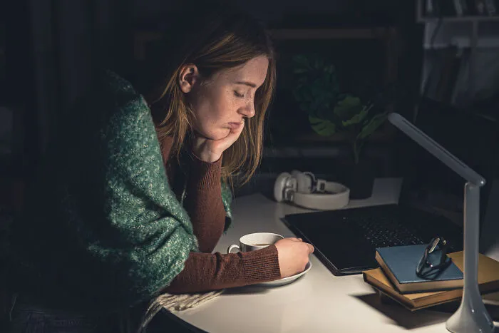 A tired woman sits at her desk with coffee, reflecting on the challenges known by divorced people