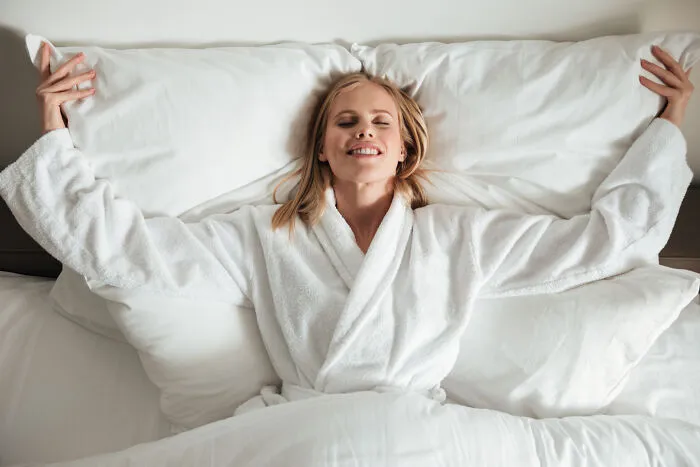Happy woman stretching in bed on fluffy pillows, learning new facts