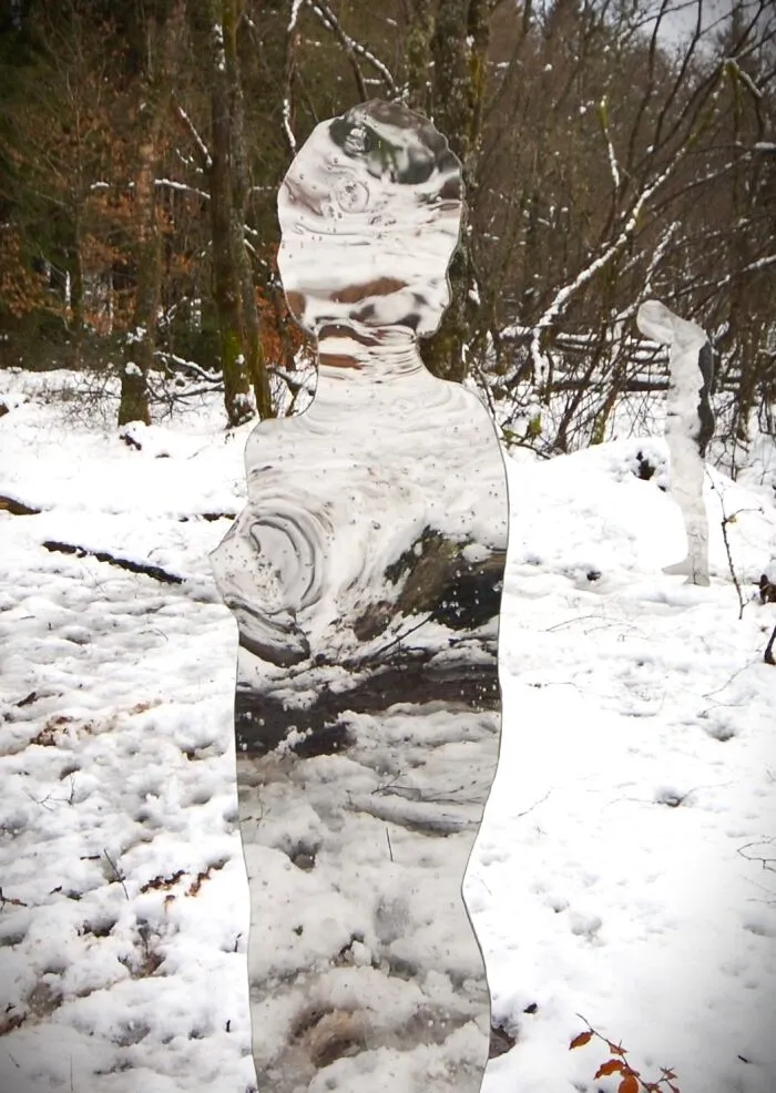 Mirrored human silhouette sculpture blending into a snowy forest background