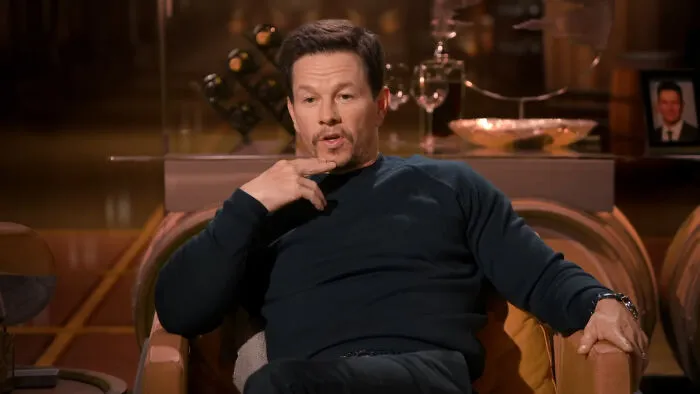 Mark Wahlberg sitting in a chair holding his chin during a celebrity encounter interview