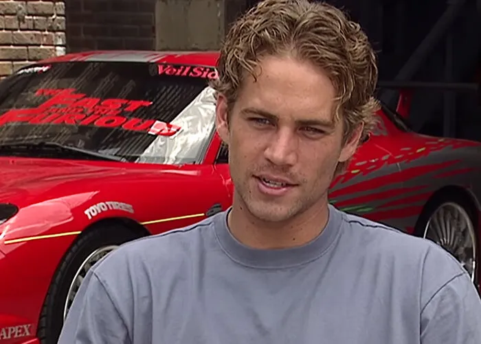 Paul Walker posing in front of a red sports car for celebrity encounters.