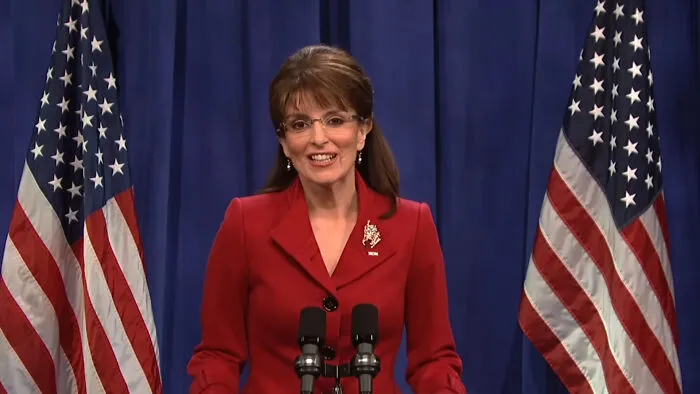 Tina Fey impersonating Sarah Palin behind a podium flanked by American flags