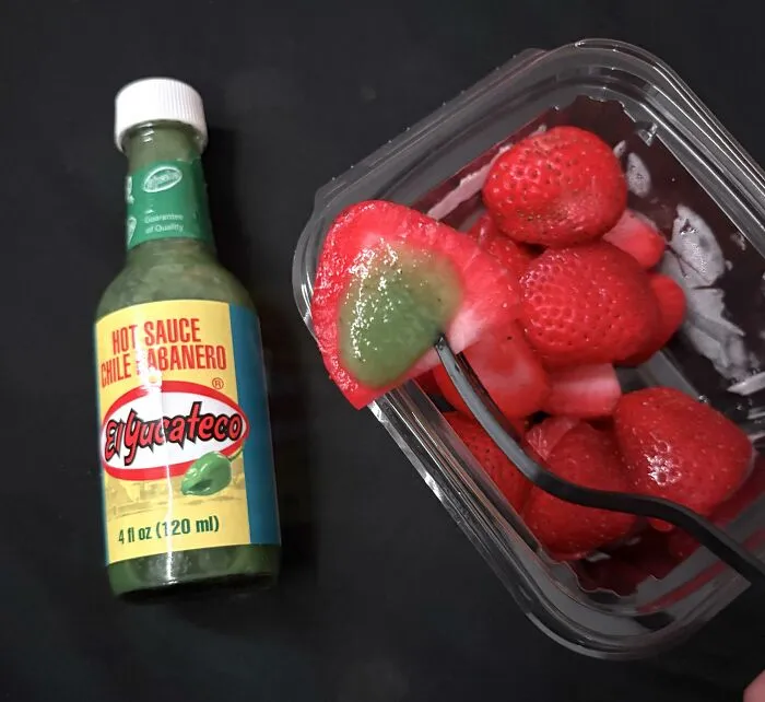 A slice of fresh red strawberry topped with green habanero hot sauce, highlighting bizarre food combinations