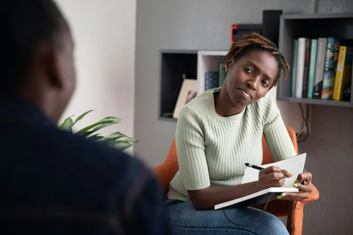 An African American woman takes notes in a notebook during an interview or therapy session at work.