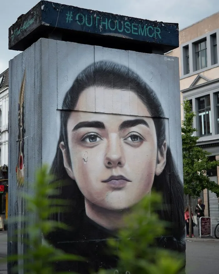 A large mural of a girl's face on a building, with '#OUTHOUSEMCR' above, hinting at Hollywood secrets.