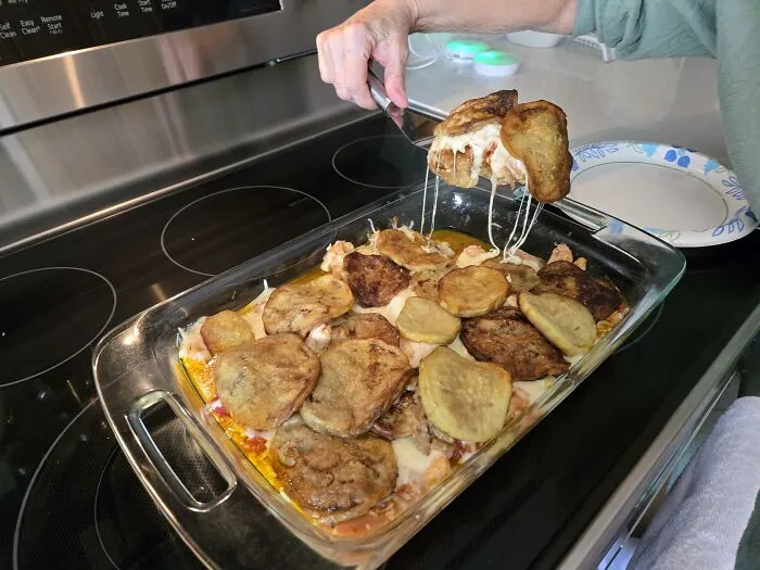 A person lifting a slice of cheesy potato casserole, an example of unusual food combinations