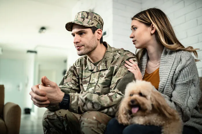 Soldier in uniform talking to woman sitting with dog indoors