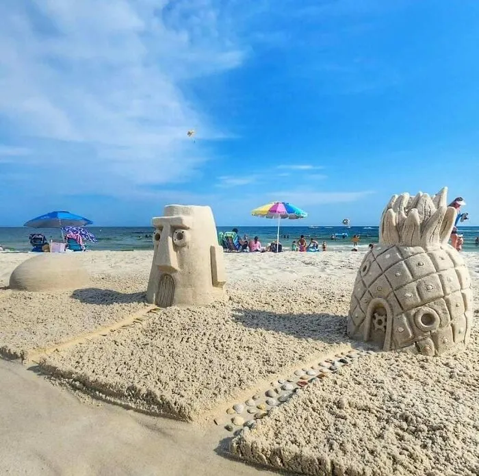 Sand sculptures of Spongebob characters on a beach with people and umbrellas in the background, making a comfortable yet disturbing scene.