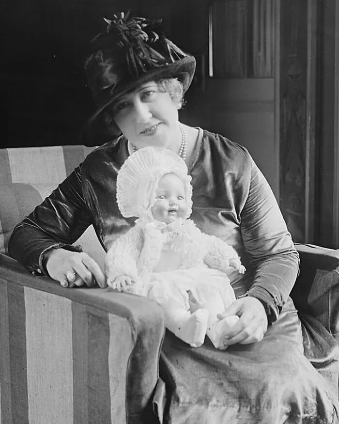 A black and white photo of a woman in a hat holding a doll, celebrating women in history.