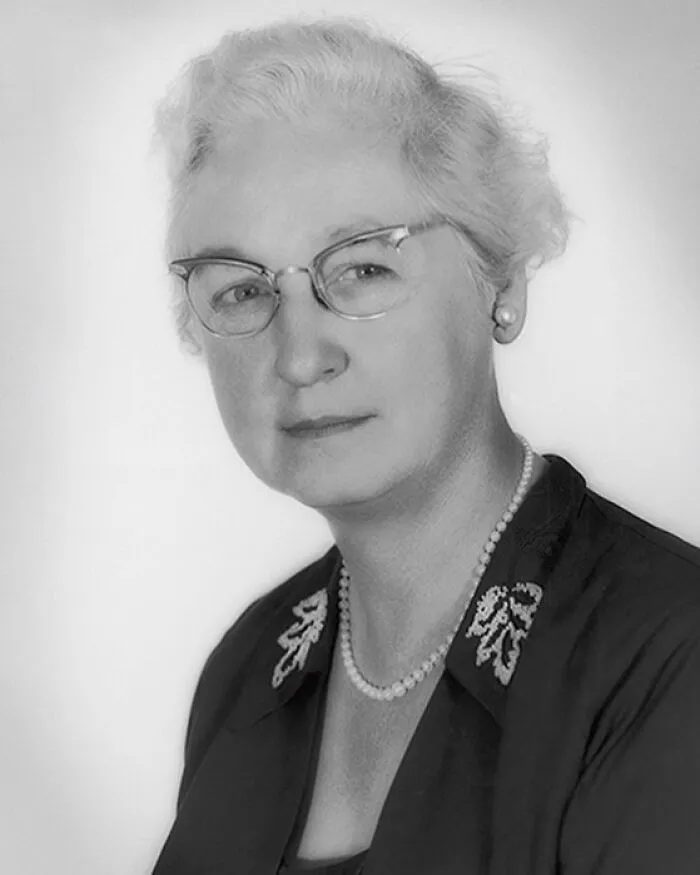 A black and white portrait of a woman wearing glasses and a pearl necklace, representing women in history.