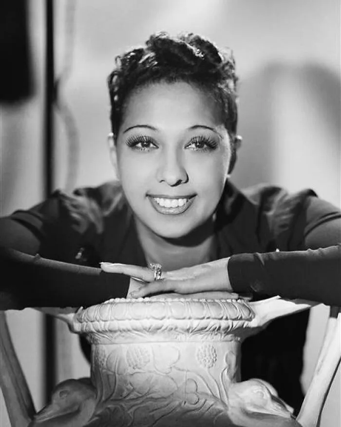 Black and white portrait of a smiling woman with dark curly hair and a ring, highlighting women in history.