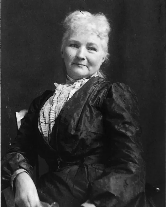 Black and white portrait of an older woman with light hair, wearing a dark ruffled dress, for women in history.