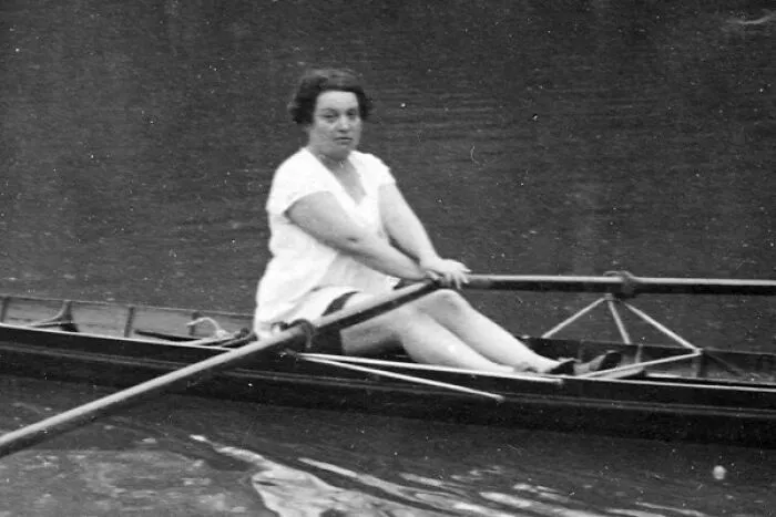 Black and white photo of a woman in a white dress rowing a boat, representing women in history.