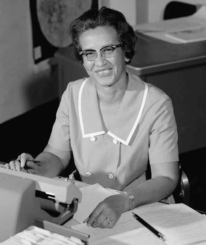 A black and white photo of a smiling woman at a desk with a typewriter, highlighting women in history.