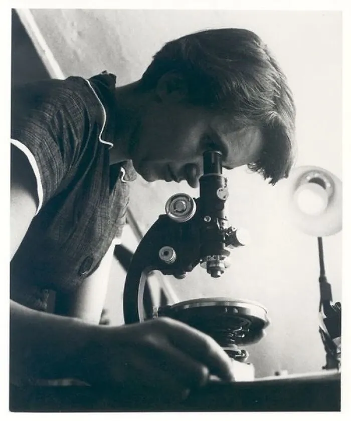 A woman in history looks into a microscope, focused on scientific discovery.