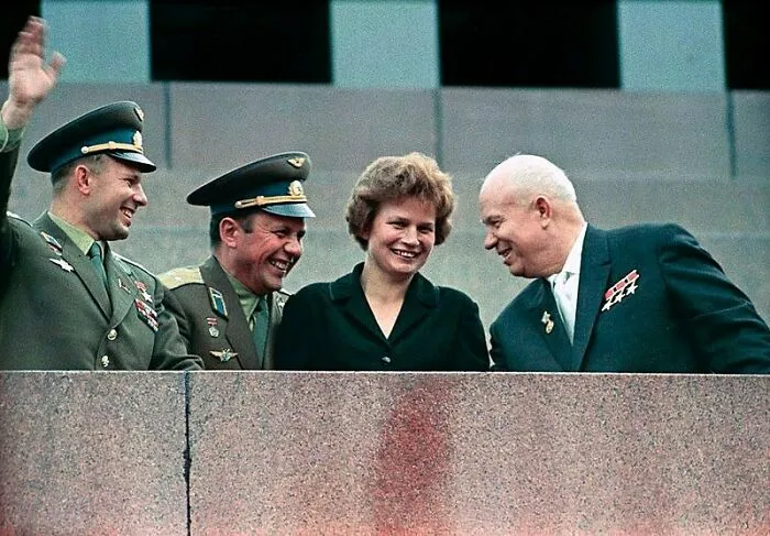 A woman in history smiles alongside two male astronauts and a political leader.