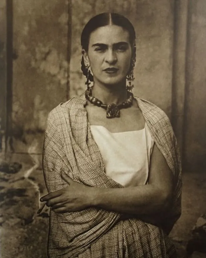 A prominent woman in history, Frida Kahlo, gazes directly with a serious expression.