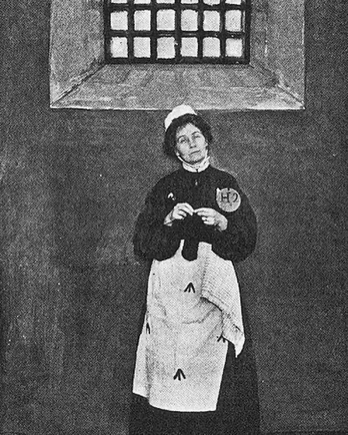 A black and white photo of a woman in a uniform, a dedicated suffragette among Women in History, standing in a jail cell, symbolizing her fight for women's rights.