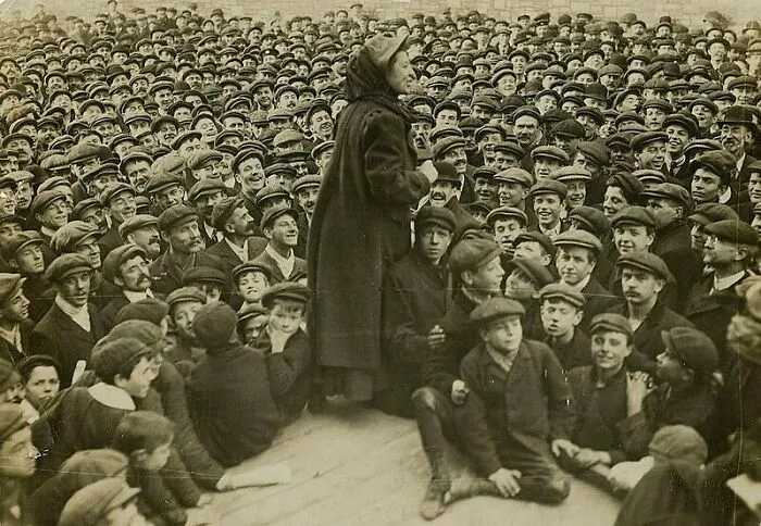 A woman addresses a large crowd of men and boys in flat caps, a powerful image of Women in History.