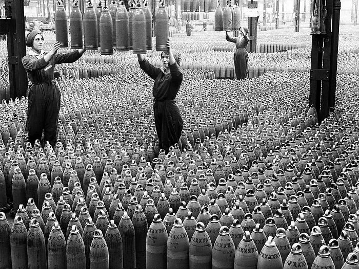 Women-In-History working in a factory, moving large shells on an assembly line.