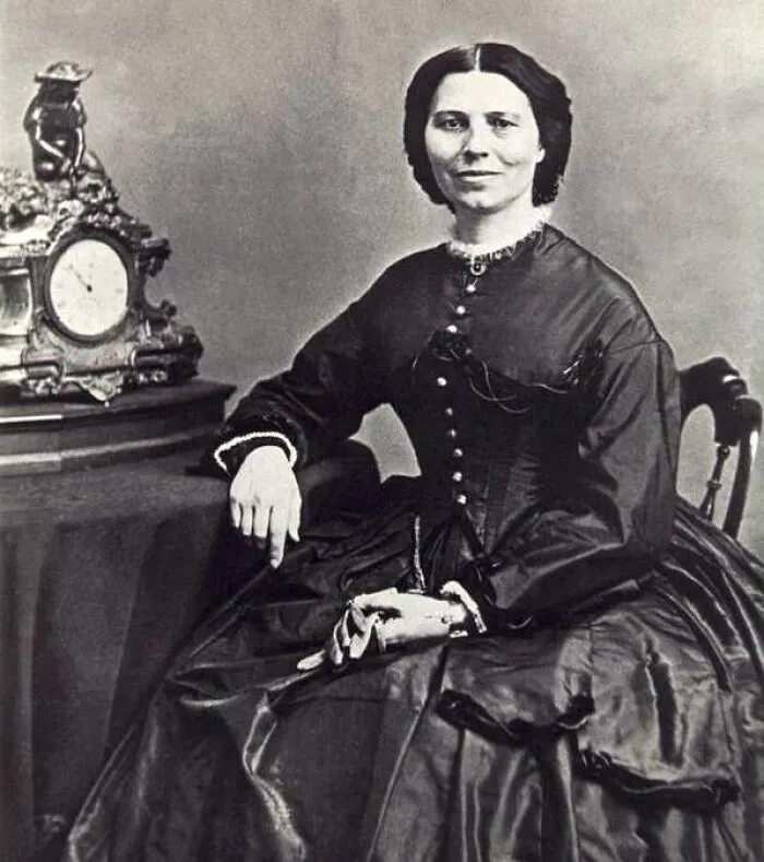 A black and white portrait of Clara Barton, a significant Women In History, seated beside an ornate clock.