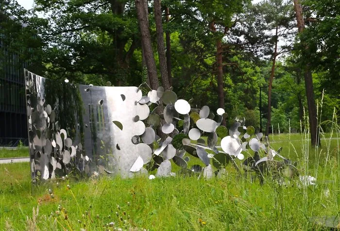 Reflective sculptures made of polished metal discs in a grassy park with trees behind