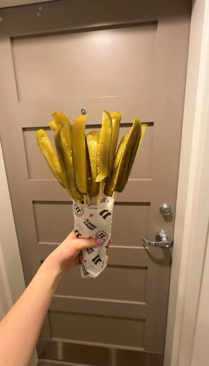 A hand holding a bouquet of pickles wrapped in paper, an unhinged image.