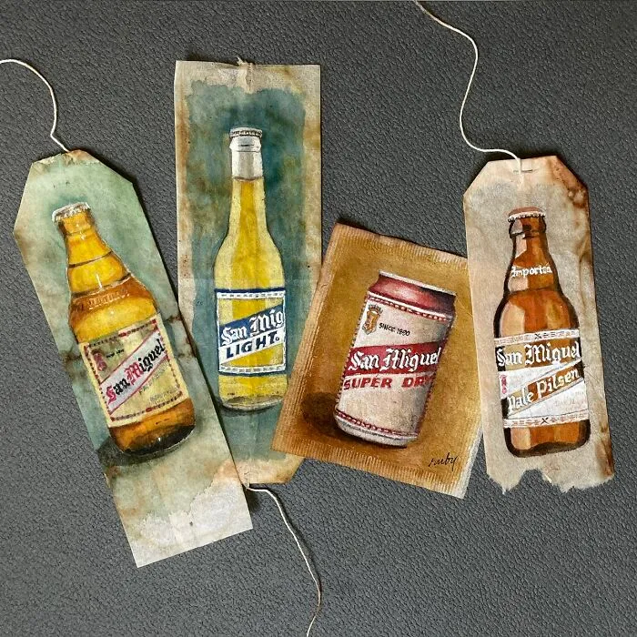 Detailed miniature paintings of beer bottles and a can on used tea bags by artist Ruby Silvious.