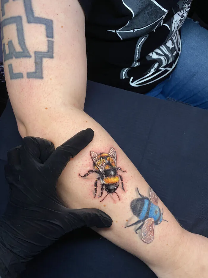 Realistic bee tattoos on forearm with artist's hand showing size comparison