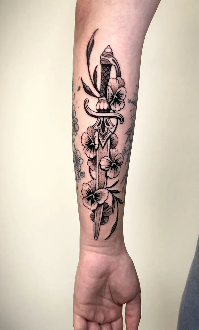 Black and gray dagger tattoo entwined with flowers on inner forearm