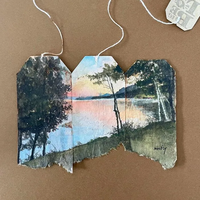 A serene lakeside landscape miniature painting across three used tea bags by artist Ruby Silvious