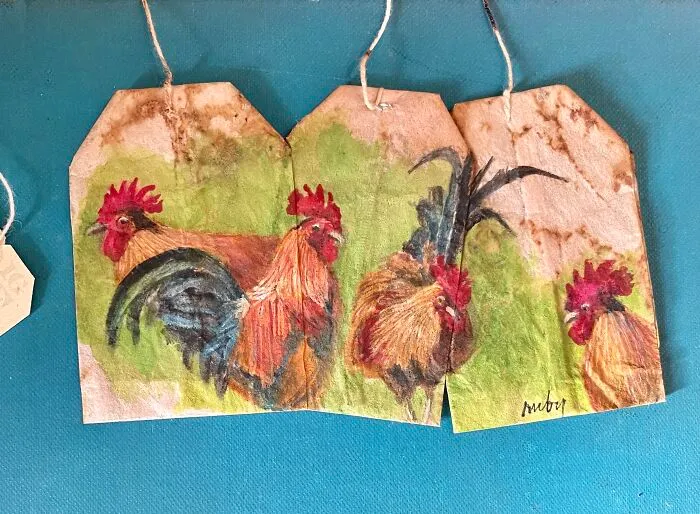 Miniature paintings of colorful roosters on used tea bags by artist Ruby Silvious