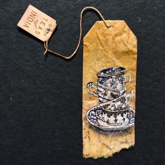 A delicate miniature painting of stacked teacups by Ruby Silvious on a single tea bag