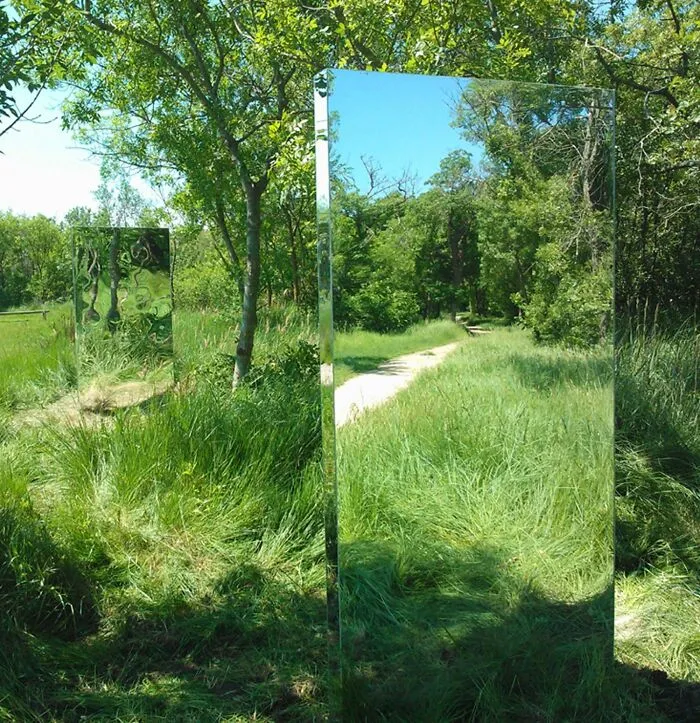 Reflective sculptures merging with tall grass in nature