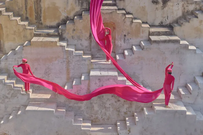 Surreal photo of three people dressed in pink with flowing fabric on stepped architecture