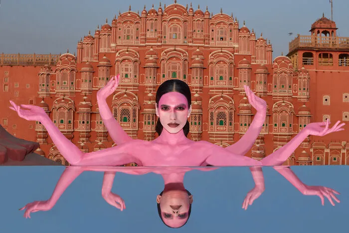 Surreal art expedition photo pink figure with multiple arms in front of ornate building with reflection