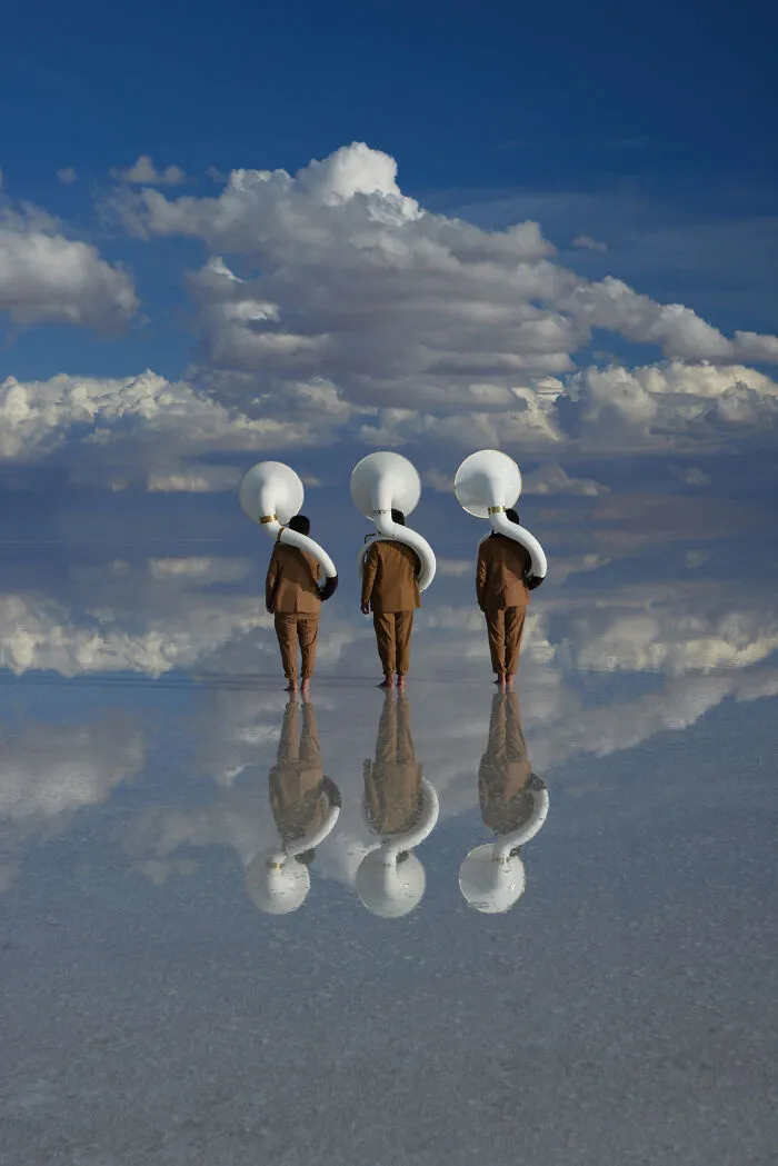 Surreal art photo of three tubists standing barefoot on reflective surface under dramatic clouds