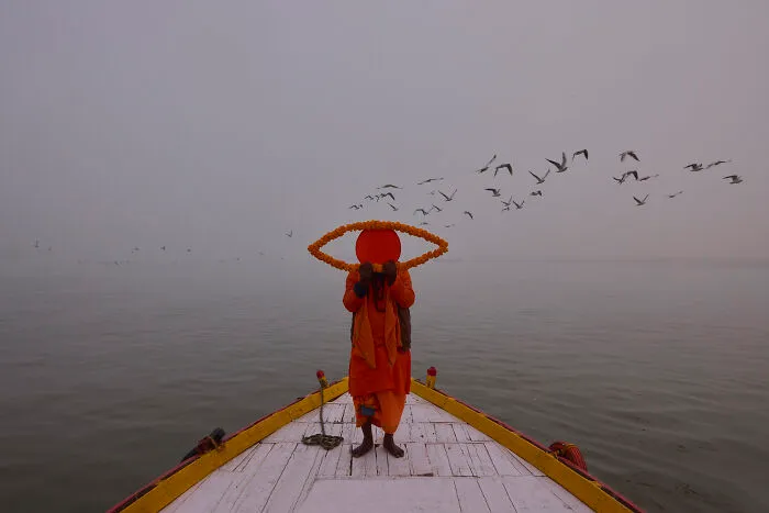 Person on boat holding orange eye-shaped object with birds flying in misty background