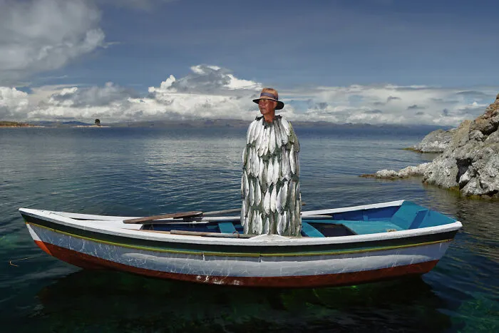Man wearing fish-covered cloak standing in boat on lake in surreal art expedition