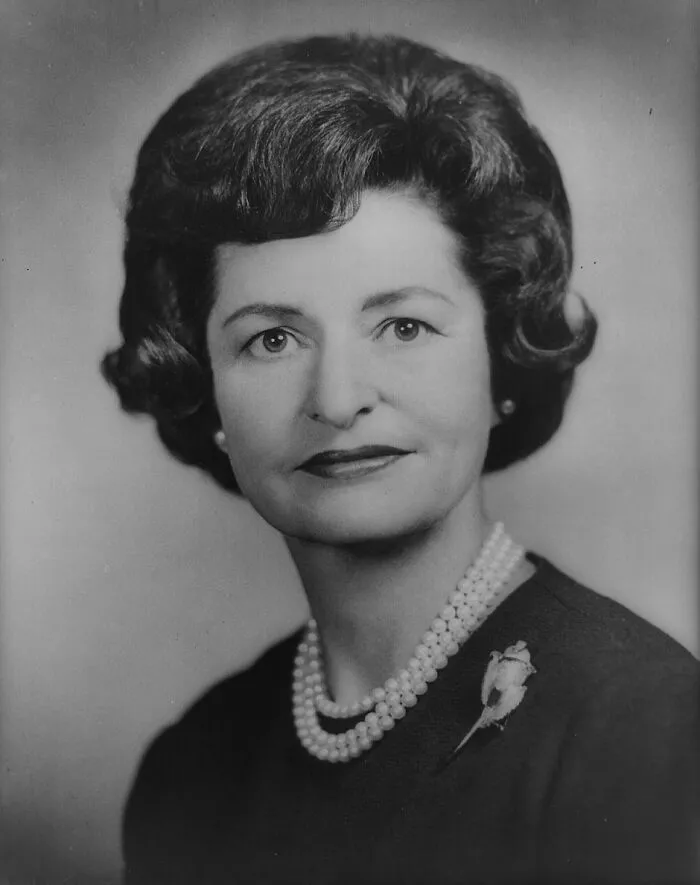 A portrait of an influential woman in history wearing a pearl necklace and brooch, looking directly at the viewer.