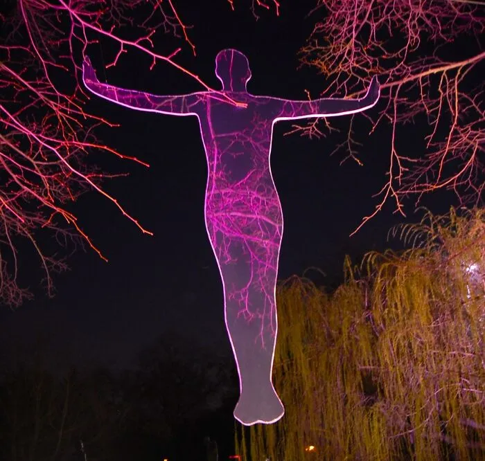 Transparent reflective figure illuminated with purple light among tree branches at night